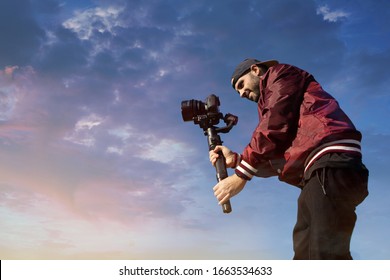 Caucasian videographer filming with cinema gimbal video dslr at sunset , professional video, video maker in event. Cinema lens on gimbal. Medium shot low angle