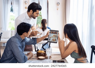 Caucasian waiter receiving order serving from customer in restaurant. Attractive server service man working, taking note, writing order from consumer with pen at table in dining room with happiness.
 - Powered by Shutterstock