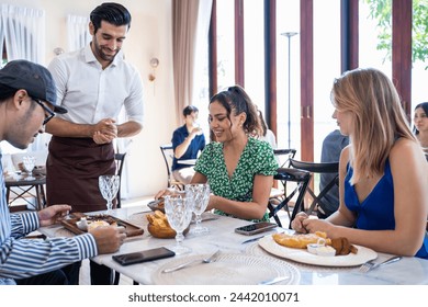 Caucasian waiter serving food to group of diverse customer in restaurant. Attractive male server service man work by delivering meal and drink to consumer at their table in dining room with happiness. - Powered by Shutterstock