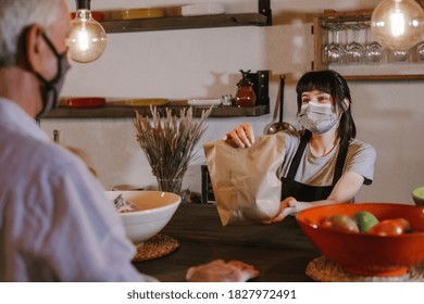 Caucasian Waitress Wearing Protective Face Mask Giving Bag To Customer In A Restaurant. Young Woman Worker Working With Take Away Orders During Corona Virus Outbreak. Concept Food And Drinks Takeaway