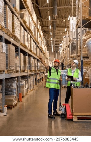 Caucasian warehouse managers walking through large warehouse distribution center discussing about increasing productivity. good teamwork, dressed in working clothes vest and hard hats