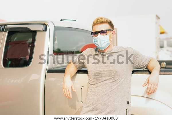 Caucasian\
wear virus facemask and stand at right of frame with placing arms\
on car while waiting for fill energy fuel into car tank, commercial\
service for benzine, diesel, gasohol,\
gasoline.