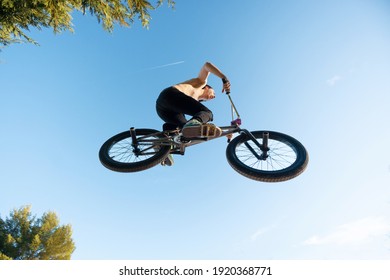 Caucasian white boy jumping with long hair shirtless with BMX bike on a mountain in the field with sand and trees blue sky sunny day - Powered by Shutterstock