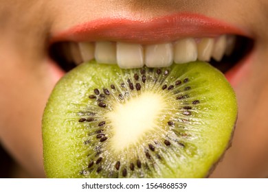 Caucasian White Woman Smiles And Bits Slice Of Kiwi. Green Fruit In Mouth. Eating Heath Food