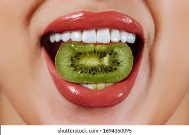 Caucasian White Woman Smiles And Bits Slice Of Kiwi. Green Fruit In Mouth. Eating Heath Food