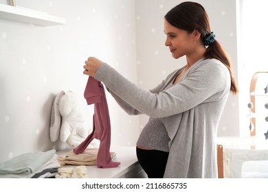 Caucasian woman in advanced pregnancy in baby's room browsing baby clothes - Powered by Shutterstock