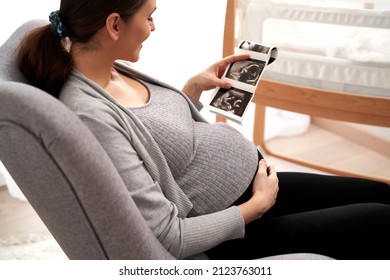 Caucasian woman in advanced pregnancy browsing ultrasound scan in baby's room