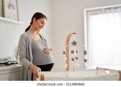 Caucasian woman in advanced pregnancy standing in the baby's room next to the crib - Powered by Shutterstock