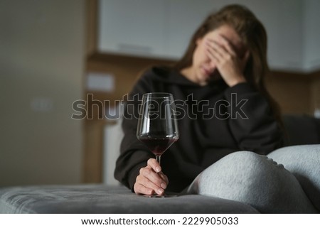Caucasian woman with alcoholism sitting at the sofa and holding glass of wine  