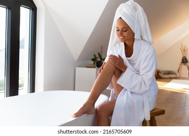 Caucasian woman in a bathrobe applying moisturizer on her leg sitting near bath tub in the bathroom. Self-care, hygiene and relaxation concept - Powered by Shutterstock