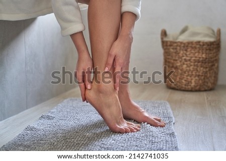 Caucasian woman in bathrobe applying moisturizing cream on heels