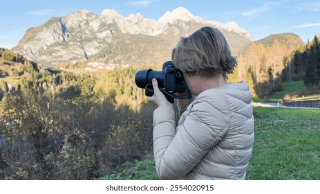 A Caucasian woman captures a scenic mountain landscape with her camera, symbolizing nature photography and exploration during autumn adventures Dolomite Alps - Powered by Shutterstock