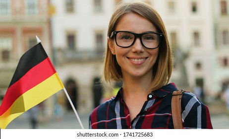 Caucasian woman in casual shirt with german flag posing on camera and smiling on the city street background.