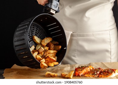 A caucasian woman chef is dumping fresh made fried potato chunks on a piece of baking paper which has three oven roasted marinated salmon fillet with basil and pepper on top. Homemade fish and chips. - Shutterstock ID 1908405760