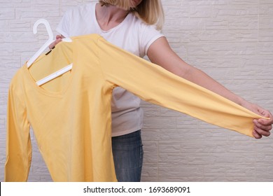 Caucasian woman choosing clothes, she is holding a hanger with yellow longsleeve , shopping, fitting and buying clothes during sale and discount concept, cheap second hand clothes for online selling.