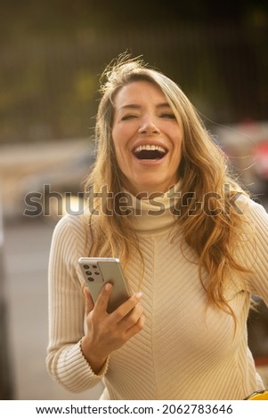 caucasian woman in the city laughing on camera with cell phone in hand