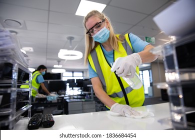 Caucasian Woman And Colleague Wearing Hi Vis Vests, Gloves, Safety Glasses And Face Masks Sanitizing An Office Using Disinfectant. Hygiene In Workplace During Coronavirus Covid 19 Pandemic.