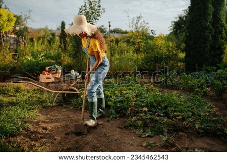 A Caucasian woman digging holes using garden shovel in her organic garden  during daytime