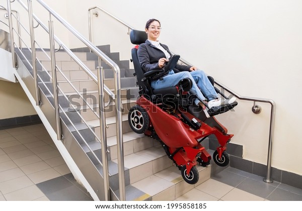 Caucasian woman in electric caterpillar\
wheelchair climbs up\
stairs.