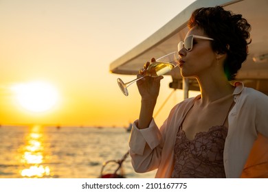 Caucasian Woman Enjoy Outdoor Luxury Lifestyle With Drinking Champagne While Catamaran Boat Sailing At Summer Sunset. Beautiful Female Relaxing Outdoor Leisure Activity With Tropical Travel Vacation