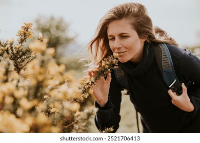 Caucasian woman enjoying nature, smelling yellow flowers. Woman with backpack, walking or hiking outdoors with nature and yellow flowers. Female hiker, nature lover woman, smelling flowers in field. - Powered by Shutterstock