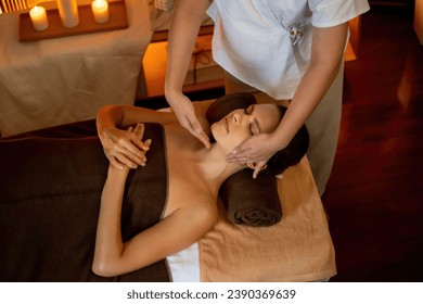 Caucasian woman enjoying relaxing anti-stress head massage and pampering facial beauty skin recreation leisure in warm candle lighting ambient salon spa in luxury resort or hotel. Quiescent - Shutterstock ID 2390369639