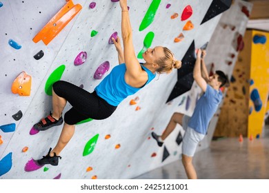 Caucasian woman exercising on wall in climbing gym during bouldering training. Young man climbing in background. - Powered by Shutterstock