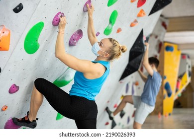 Caucasian woman in face mask exercising on wall in climbing gym during bouldering training. High quality photo - Powered by Shutterstock