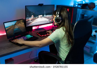 Caucasian Woman Gamer With Headphones Using A Gaming Laptop And Computer PC At The Same Time To Play An Online Video Game In Her Bedroom