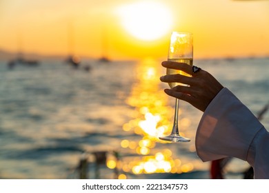 Caucasian woman hand holding champagne glass relax and enjoy luxury outdoor lifestyle while travel on catamaran boat yacht sailing in the ocean at sunset on summer beach holiday vacation trip