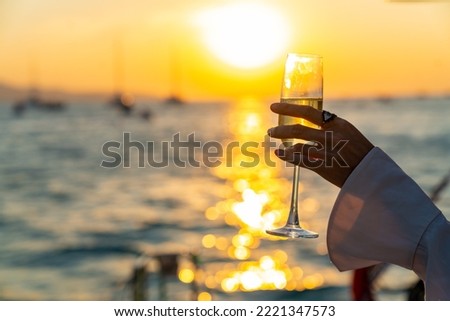 Caucasian woman hand holding champagne glass relax and enjoy luxury outdoor lifestyle while travel on catamaran boat yacht sailing in the ocean at sunset on summer beach holiday vacation trip