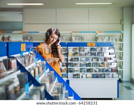 caucasian woman with headphones, choosing cd in music shop. Horizontal shape, front view, waist up, copy space