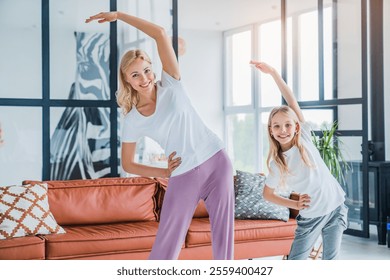 Caucasian woman with her daughter doing morning fitness exercises at home. Vitality concept. Cute cheerful joyful with long hair schoolgirl and slim sportive mom are doing stretching exercises in room - Powered by Shutterstock