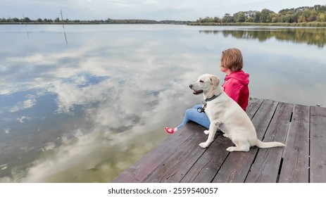 A Caucasian woman and her dog enjoy a peaceful lakeside moment, symbolizing relaxation and companionship on a serene day - Powered by Shutterstock