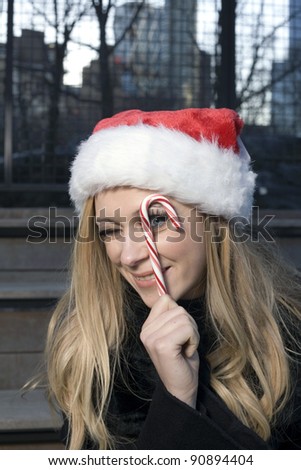 A Caucasian woman holding a candy cane and wearing a Santa hat.