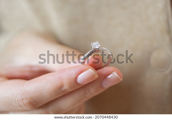 Caucasian woman holding simple solitaire diamond\
engagement ring white gold\
