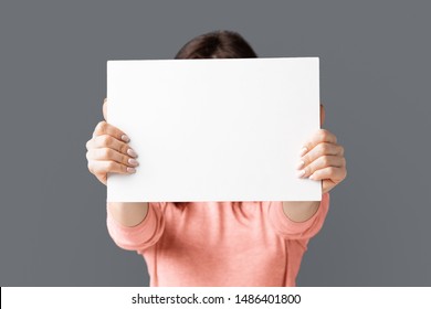 Caucasian Woman Holding White Blank Card In Front Of Her Face, Grey Studio Background