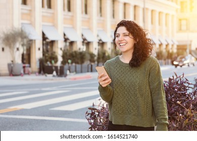 Caucasian woman holds her cell phone while waiting for ab uber in the City - Warm light in the daytime - Concept happy using technology