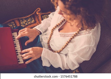 Caucasian woman at home relaxing singing a little toy piano sitting on the sofa -people enjoying indoor leisure activity -  artist creative concept adult female viewed from above