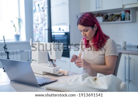 Caucasian woman learning to sew from a video tutorial while sitting in the kitchen. Home hobby for an online lesson