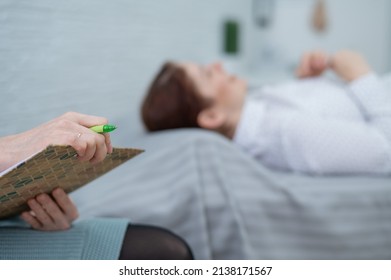 A caucasian woman lies on a couch and expresses her feelings, while a psychologist makes notes on a tablet. 