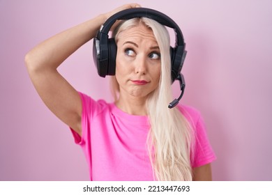 Caucasian Woman Listening To Music Using Headphones Confuse And Wonder About Question. Uncertain With Doubt, Thinking With Hand On Head. Pensive Concept. 