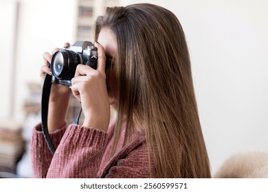 Caucasian woman with long blonde hair using a vintage camera indoors. Wearing a pink sweater, she captures a photo in a bright, cozy room. - Powered by Shutterstock