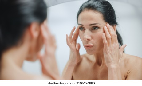 Caucasian Woman Looking In Mirror, Touching Beautiful Face, Soft Skin. Elderly Lady With Lush Black Hair. Female Beauty, Dignity, Grace. Sensual Wellness And Organic Skincare Products. Portrait Shot