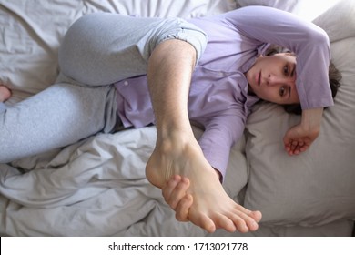 Caucasian Woman Looking On Her Hairy Leg Resting On Bed At Home. She Can Not Do Depilation In Quarantine. Top View.