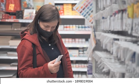 Caucasian Woman In A Mask Against The Virus Chooses Tubes Of Paint For Drawing In A Store. The Concept Of Hobby, Craft And Design