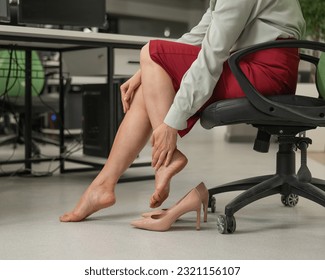 Caucasian woman massaging her tired legs while sitting in the office. Cropped.  - Powered by Shutterstock