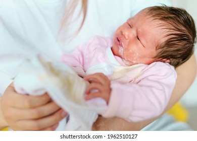 caucasian woman mother hold newborn infant girl vomiting milk after eating - baby overfeeding puke milk in hands of her mother at home - new life nursing and growing up concept
