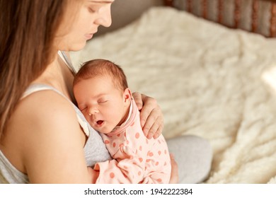 Caucasian Woman Mother Sitting On Bed And Holding Sleepy Baby Infant In Arm, Female Touching Kid's Back, Mommy Looking At Her Kid And To Calm Baby Down And Sleep.