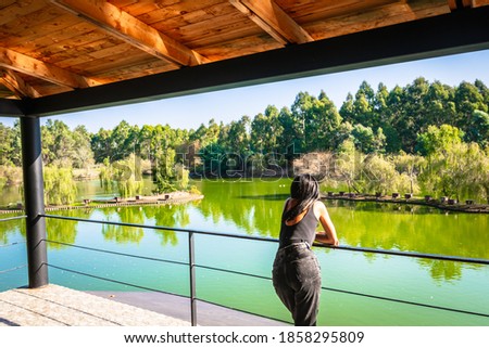 Caucasian woman on viewpoint platform looks left to green nature and lake in the background. Blank space image. Dendrological park.Georgia.